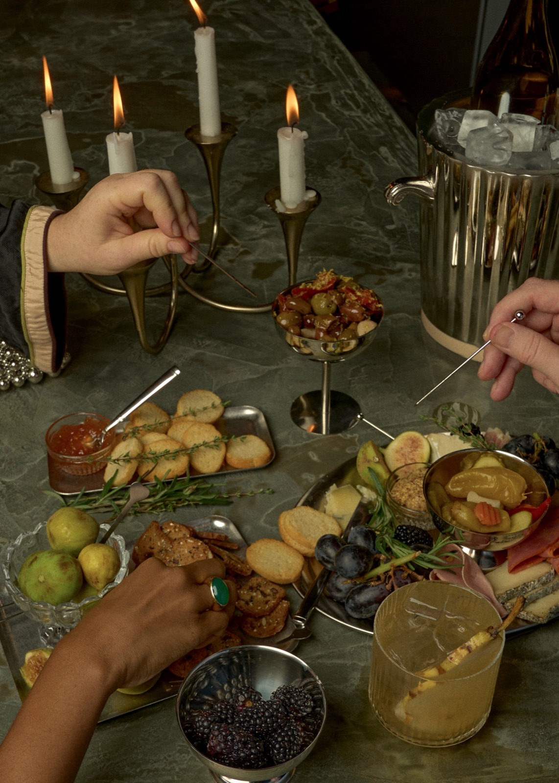Hands reaching across a candlelit spread of small plates.
